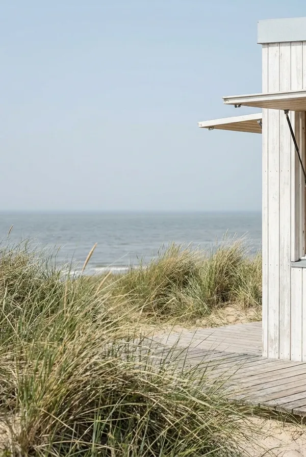Weiße Holzbude mit aufgeklappter Verkaufsklappe am Dünenweg, dahinter Strandhafer und Meer